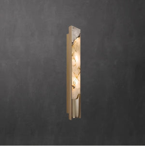 The Luxury Marble Wall Sconce features a gold frame and a marbled glass cover that emits a soft, inviting light. Mounted on a dark textured wall, this fixture brings timeless elegance to any interior space.