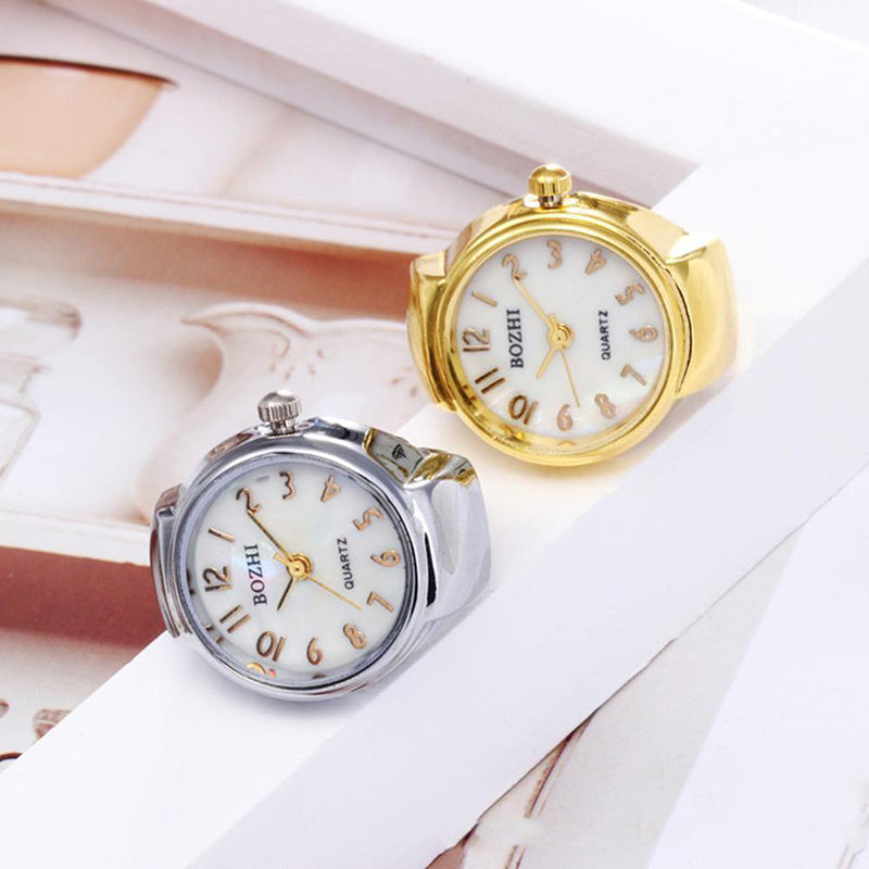Two Vintage Ring Watches with pearlescent dials and gold numerals—one featuring a gold band, the other a silver band—evoke personalized luxury as they're displayed on a white geometric surface.