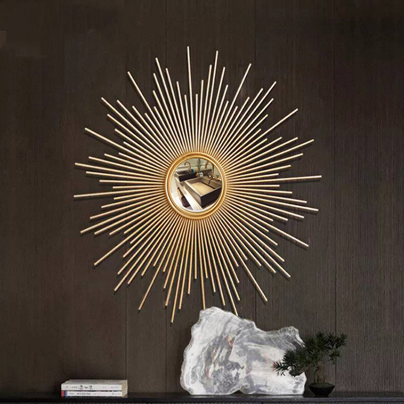 The Luxe Sunray Wall Mirror with gold rays adds a statement touch to interiors, mounted on a dark wall above a console table styled with a decorative stone, a small plant, and a stack of books.