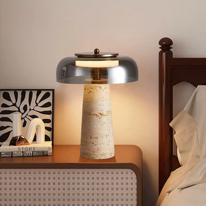 The Mushroom Desk Lamp, featuring a natural stone base and a metal shade, sits on a nightstand by the bed, providing organic desk lighting beside a decorative book and an art piece.