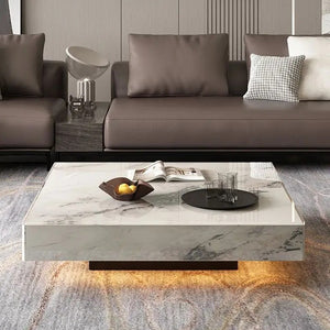 A modern living room features the Modern Luxe Coffee Table with a book, a fruit bowl, and a tray with glasses, placed in front of a brown sofa adorned with cushions.