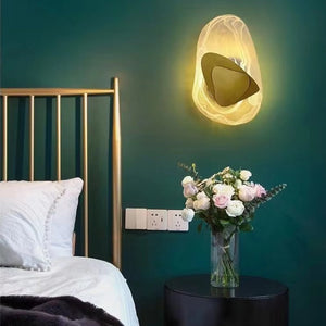 A bed featuring a gold headboard and white bedding sits beside a round table topped with a vase of flowers, while the Luxury Crystal Wall Lamp casts light across the green wall.