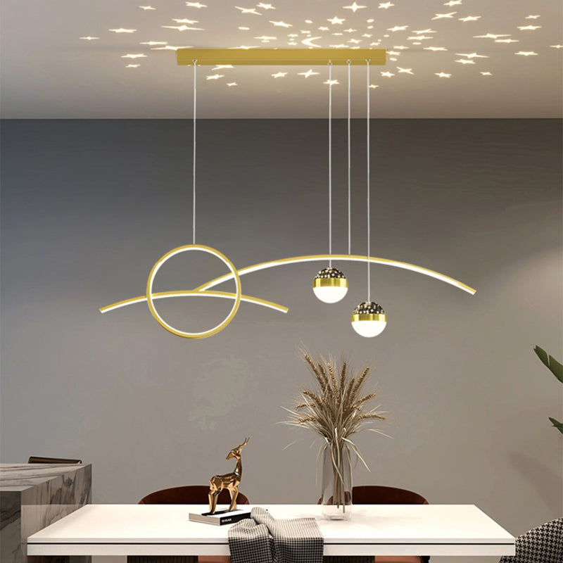 A modern dining room is illuminated by the Stellar Pendant Light, which casts star-like reflections. The table is adorned with a small gold deer ornament and dried plants, adding celestial accents.