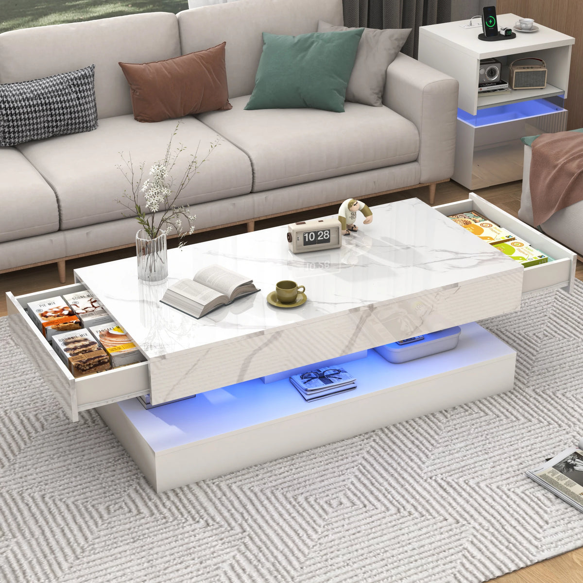 The Premium Coffee Table features a modern marble-gloss finish with open side drawers for snacks, books, cups, and decor, perfectly accenting a living room alongside a sofa and shelf.