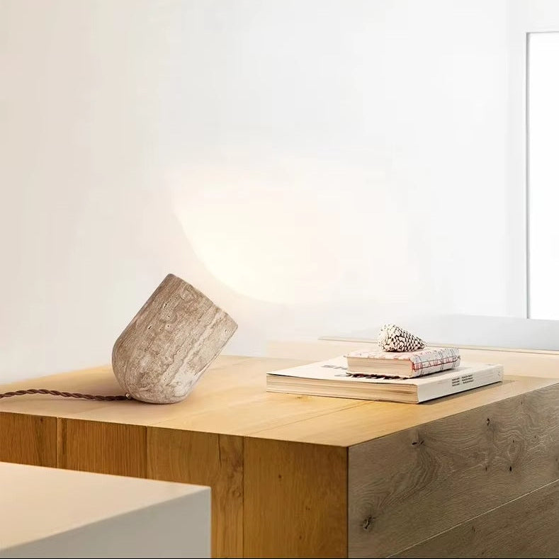 A Natural Stone Lamp, two books, and a seashell rest on a light wood table in a minimalist, well-lit room with white walls.
