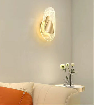 A Luxury Crystal Wall Lamp is mounted above a petite table decorated with white flowers in glass vases, next to a cream sofa featuring an orange and cream pillow, adding an elegant focal point to this minimalist room.