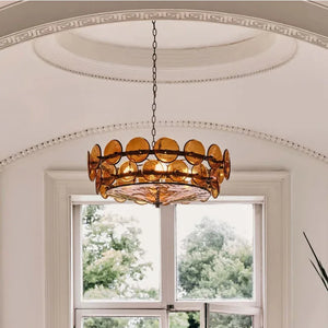 An Italian Retro Pendant Light with amber glass discs hangs from a chain in a room with white walls and a large window overlooking lush green trees.