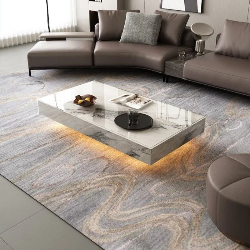 Modern living room with the Modern Luxe Coffee Table (underlit, minimalist), brown leather sofa, round ottoman, and abstract-patterned rug—ideal for modern interiors.