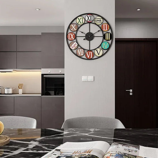A modern kitchen and dining area with grey cabinets features the Nordic Color-Ring Wall Clock, which displays vibrant Roman numerals and the word "ONE" for the number 1.