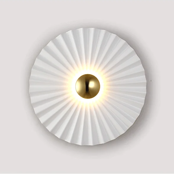 The Origami Circle Wall Light features a round LED design with a pleated white shade and a central metallic gold disk, making it a perfect gold accent wall light for any space.