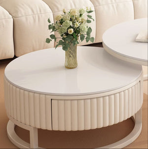 The Luxury Round Coffee Table Set, with its white minimalist design and ribbed base, holds a vase of white and light green flowers elegantly in front of a beige sofa.
