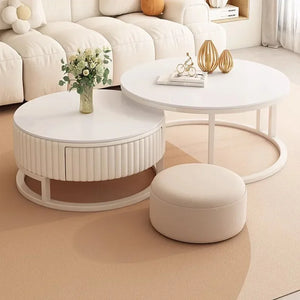 The Luxury Round Coffee Table Set, featuring a minimalist table with a drawer and vase of flowers, plus a small ottoman, is arranged on a beige carpet in front of a white sofa.