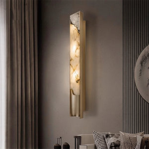 The Luxury Marble Wall Sconce features a tall, rectangular design with a marble-inspired finish, casting a warm glow in a modern living room adorned with vertical wall paneling and floor-length curtains in neutral tones.