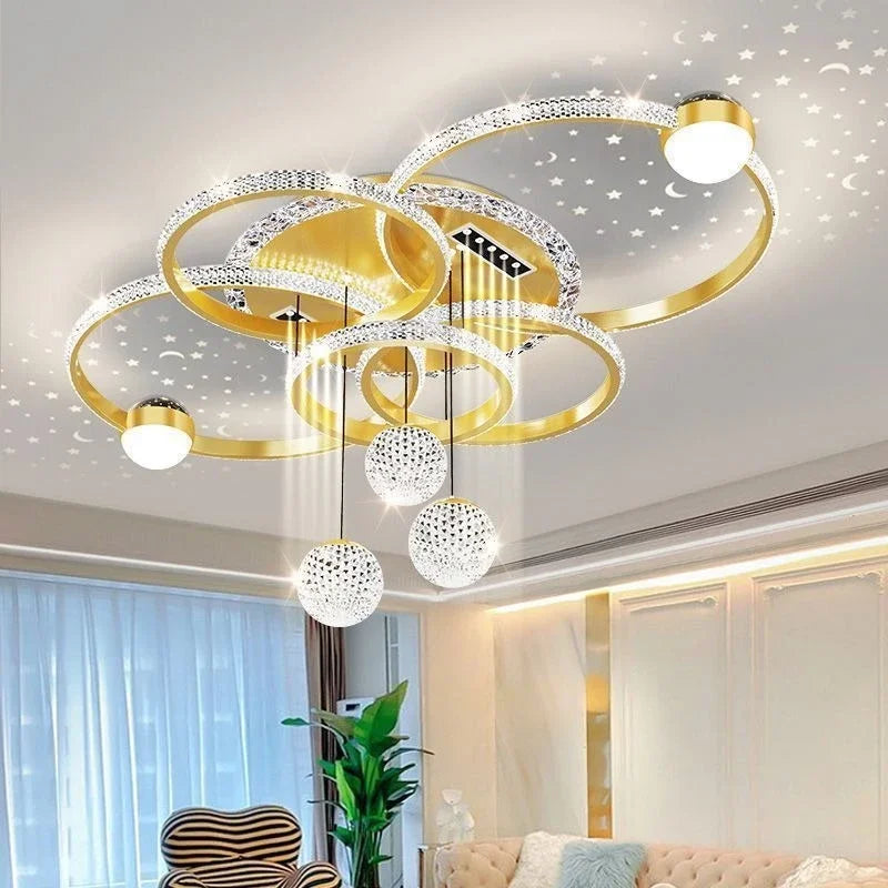 The Elegant Multi-Ring Ceiling Light features gold rings, crystal spheres, and LED bulbs, casting star and moon patterns on the white ceiling of a contemporary living room.