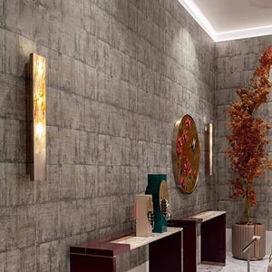 Modern hallway with textured gray walls, Luxury Marble Wall Sconces casting a warm glow, decorative vases on marble tables, a round wall art piece, and a tall plant with orange leaves in the corner.