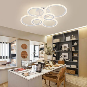 Modern, well-lit office with decorative shelves, art pieces, books, and a Smart Circle Ceiling Light featuring adjustable brightness. Large desk holds magazines, baskets, and a vase with dried flowers.