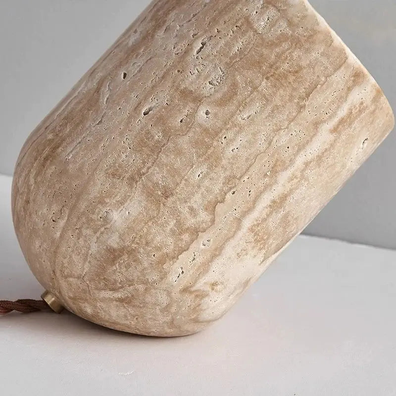 A close-up of a beige, stone-textured cup with a rounded shape, resting on its side on a light gray surface—its organic finish reminiscent of the Natural Stone Lamp.