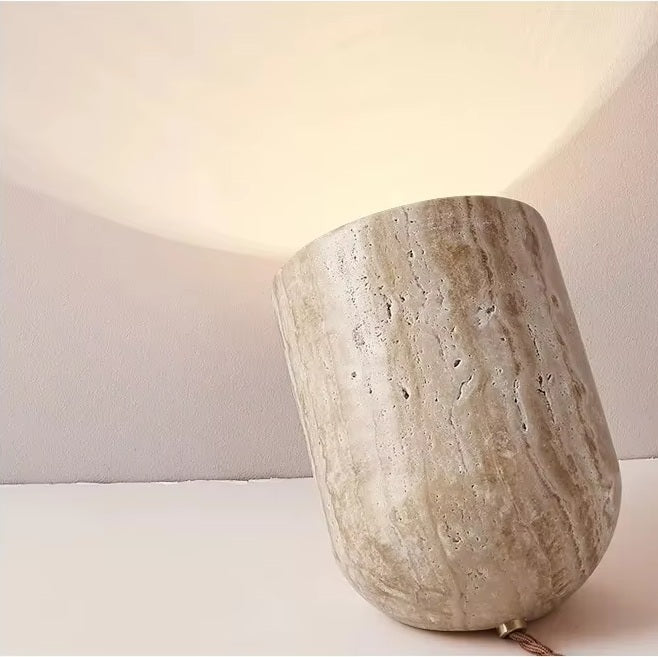 The Natural Stone Lamp, a sculptural table lamp made from yellow cave stone, is angled to cast a gentle, upward glow onto a white wall and ceiling.