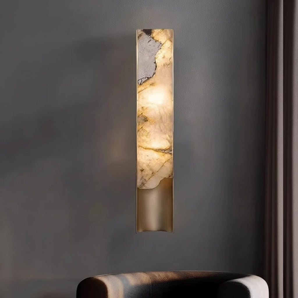 The Luxury Marble Wall Sconce, featuring a marble-like panel, emits warm light and is mounted on a gray wall above a dark upholstered chair.