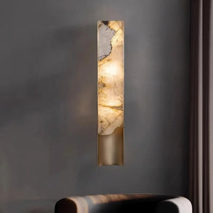 The Luxury Marble Wall Sconce, featuring a marble-like panel, emits warm light and is mounted on a gray wall above a dark upholstered chair.