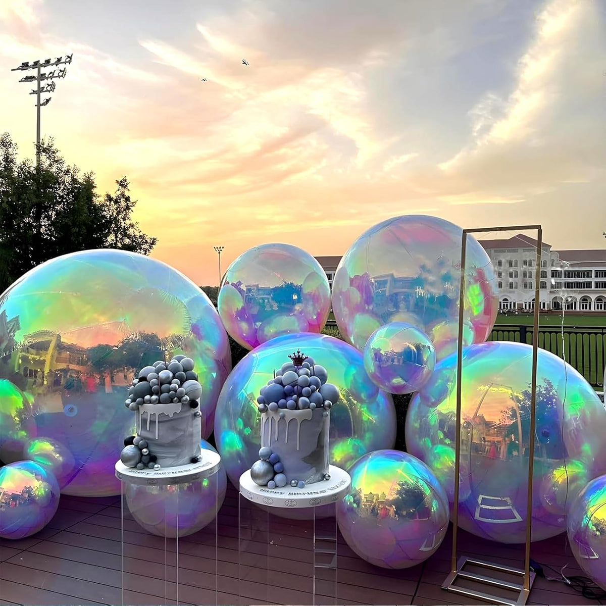 Two gray cakes with sphere decorations sit on clear stands before large Inflatable Gazing Balls at an outdoor venue during sunset, bringing a whimsical touch to the garden decor.