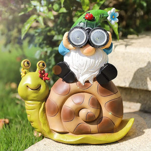 Perched atop a large snail with a flower on its head, the whimsical Solar Gnome Snail Light features a charming gnome holding binoculars. Perfect for adding personality to your outdoor decor, this unique garden solar light illuminates your space, while lush grass and stone steps provide an enchanting setting.