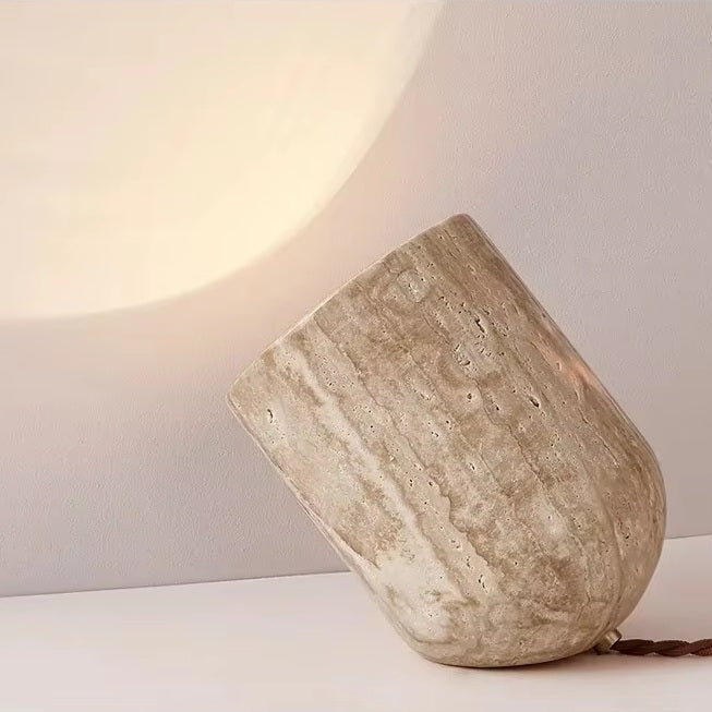 The Natural Stone Lamp, sculptural in design and crafted from yellow cave stone, rests on its side to cast a gentle, warm glow across both wall and surface. Its richly textured finish accentuates the organic elegance of the natural material, creating an inviting ambiance in any room.
