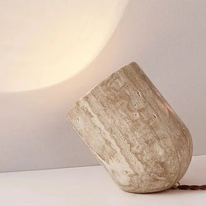The Natural Stone Lamp, sculptural in design and crafted from yellow cave stone, rests on its side to cast a gentle, warm glow across both wall and surface. Its richly textured finish accentuates the organic elegance of the natural material, creating an inviting ambiance in any room.