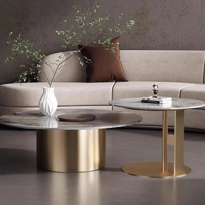 The Premium Round Coffee Table, featuring gold bases and marble tops, sits in front of a beige sofa with a white vase and decorative item. This contemporary table set brings elegance to any living space.