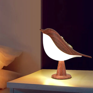 The Bird Table Lamp, with its modern design and wooden texture, emits a warm light and is elegantly placed on a bedside table. It features a touch sensor for effortless control.