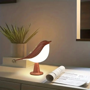 The Bird Table Lamp casts a warm glow on the desk, nestled next to a rolled-up paper and a potted plant.