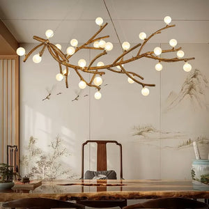 The Branch Pendant Light, featuring a branch-like design and glass orb shades, hangs above a wooden table in a room decorated with nature-themed wall art.