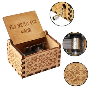 The Wooden Music Box features a handcrafted wooden design with an open lid that displays the song title "Fly Me to the Moon." Close-up insets highlight the hand-cranked winding mechanism and intricate carvings, offering classic melodies with an elegant touch.