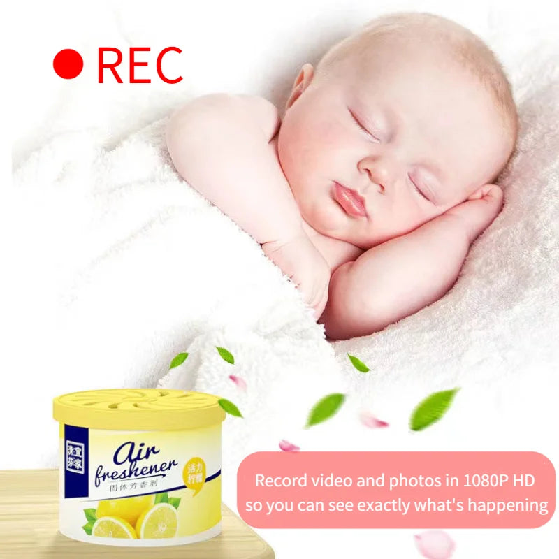 A baby sleeps wrapped in a blanket with a container of air freshener nearby. A red "REC" icon is displayed in the top left corner. The text reads: "Record video and photos in 1080p HD so you can see exactly what's happening with this Fake Decorative Display SpyCam.