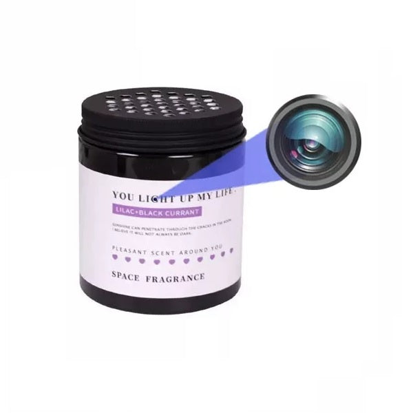 A cylindrical black container labeled "Lilac + Black Currant" with the text "You Light Up My Life" features a lens on the front, revealing it to be a Cylindrical Display SpyCam with 1080p HD resolution. This cleverly disguised surveillance device offers wireless connectivity for discreet monitoring.