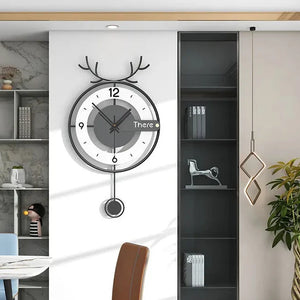 An Antler-like Wall Clock with a small pendulum is elegantly hung on a white wall beside a bookshelf and a brown chair, adding a nature-inspired touch to the decor.