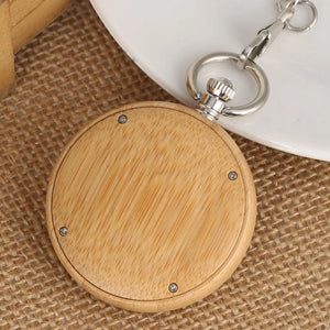 A Personalized Natural Minimalist Silver Bamboo Wood Pocket Watch Taschenuhr with a metal crown and clip rests on burlap fabric beside a white plate.