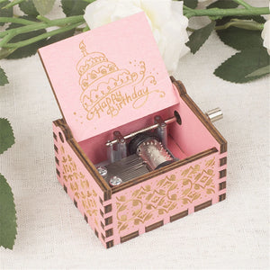 A dainty pink "Happy Birthday Music Box" featuring a cake motif on the lid, encircled by white flowers—an ideal birthday gift.