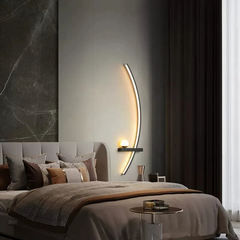 Modern bedroom with a neutral color scheme, featuring a bed with multiple pillows, an elegant Arc Wall Sconce for stylish lighting, a small round side table, and floor-to-ceiling curtains.