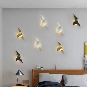 Bedroom with a wooden headboard bed, grey pillows, and a black lamp on the side table. The wall behind the bed features Modern Flying Bird Wall Sconces in white, gold, and black colors.