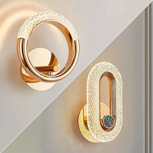 Two Luxury Wall Sconces featuring gold metallic finishes and textured circular designs. The left light is ring-shaped, while the right light has an elongated oval design, perfect for indoor lighting.