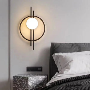 The Circular Wall Sconce with Dual Vertical Rods is mounted beside a bed with white bedding and a gray headboard. A terrazzo nightstand sits next to the bed.