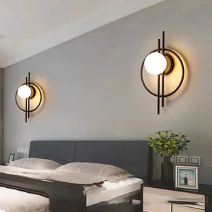 Modern bedroom featuring a dark upholstered bed, two Circular Wall Sconces with Dual Vertical Rods highlighting circular designs, and a nightstand holding a small potted plant and framed photo.