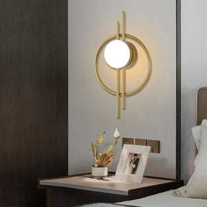 A Circular Wall Sconce with Dual Vertical Rods is mounted above a nightstand. The nightstand holds a photograph, a small vase of dried flowers, and is positioned next to a neatly made bed.