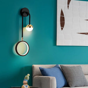 Modern living room with a teal wall, abstract wall art, and a stylish Nordic Hanging Circle Wall Light. The beige couch is complemented by blue and black-and-white pillows. A small decorative figure sits on the armrest, perfectly accentuating the geometric forms throughout the space.