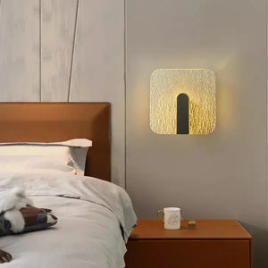 A modern bedroom with a brown leather headboard, crisp bedding, a bedside table holding a mug and phone, and the Beautiful Wall Sconce featuring minimalist design lighting and a textured surface.