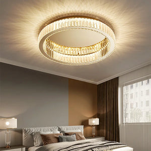 Elegant bedroom showcasing a Luxury Ceiling Circle Crystal Light that emits a warm glow, accompanied by two bedside lamps. A neatly made bed is positioned near a large window with curtains, exuding sophistication and style.