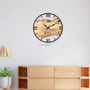 Wood Circle Wall Clock featuring black Roman numerals on a rustic wood-textured face, displayed above a light wooden cabinet, alongside a small plant and beneath a pendant light.