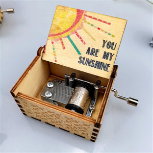 The Music Box - You Are My Sunshine features a wooden lid adorned with colorful text that reads "You are my sunshine." This Romantic Rotary Handle Music Box is elegantly crafted with an intricate star design on the front and a metal crank on the side.