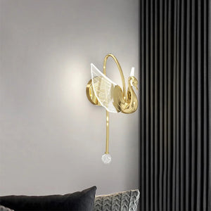 A sophisticated Swan Wall Light fixture features glowing white wings mounted on a light gray wall, positioned next to black curtains. This decorative swan sconce emits a warm glow, illuminating the surrounding area and adding a touch of elegance to your indoor lighting.